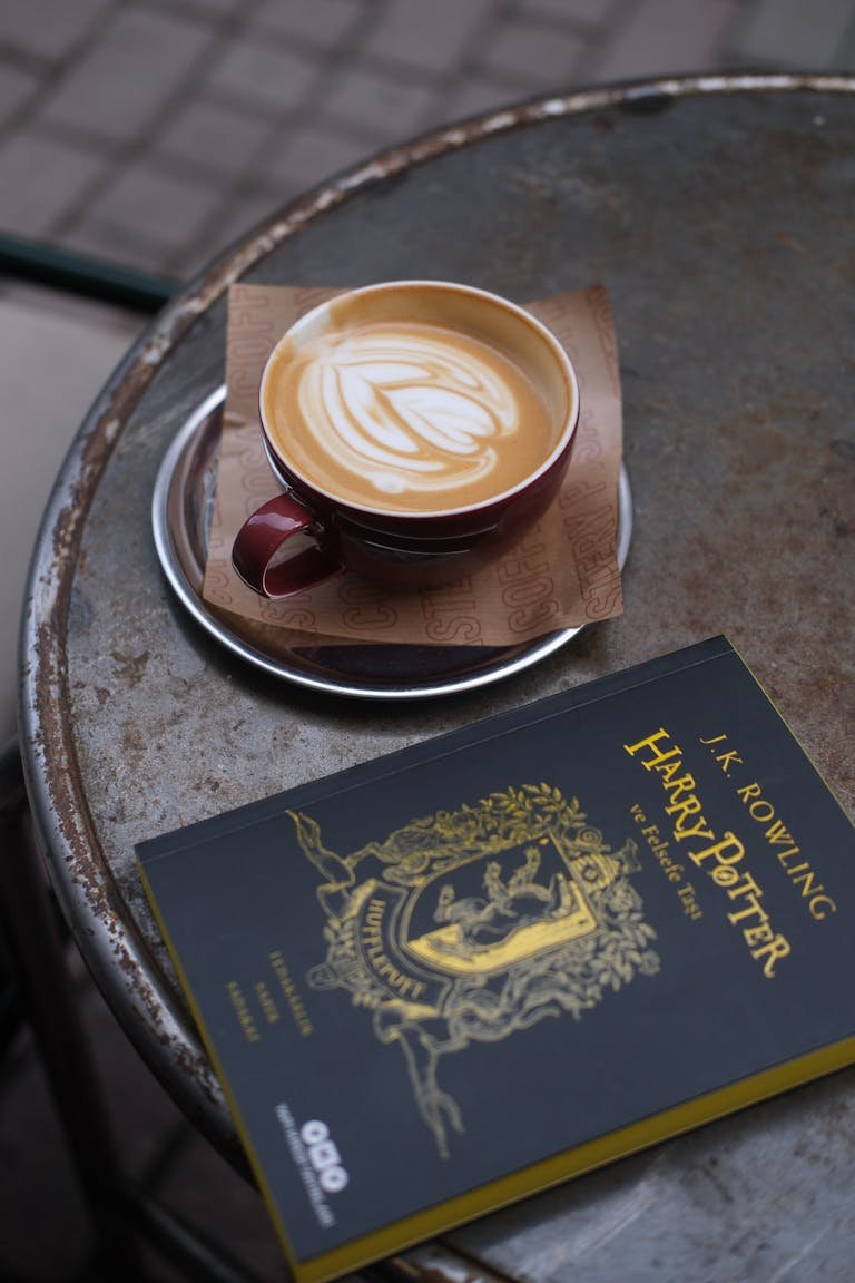 A latte with latte art beside a Harry Potter book on a rustic table.