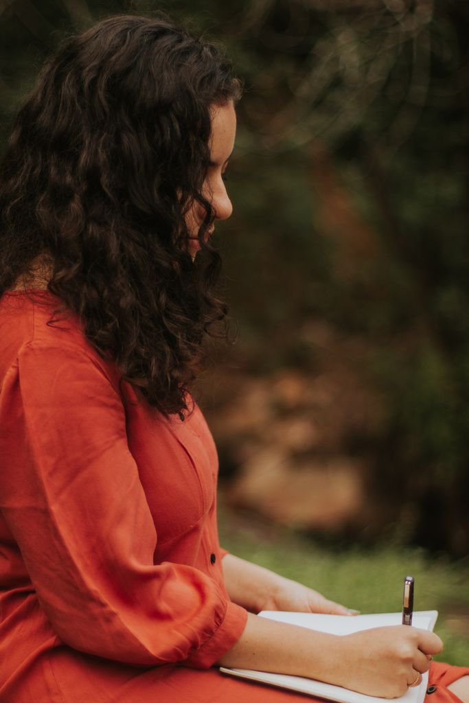 A thoughtful young woman writing in a notebook during a peaceful outdoor retreat.