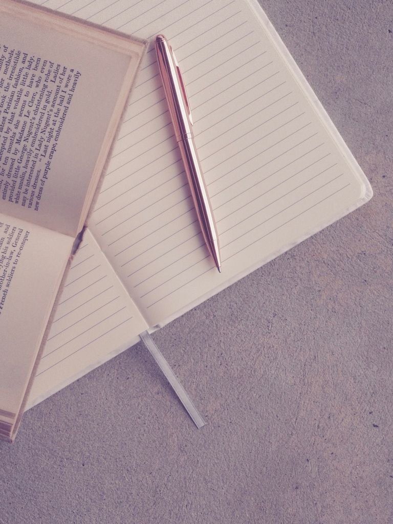 Creative flatlay featuring an open book, notebook, and pen on a textured surface.