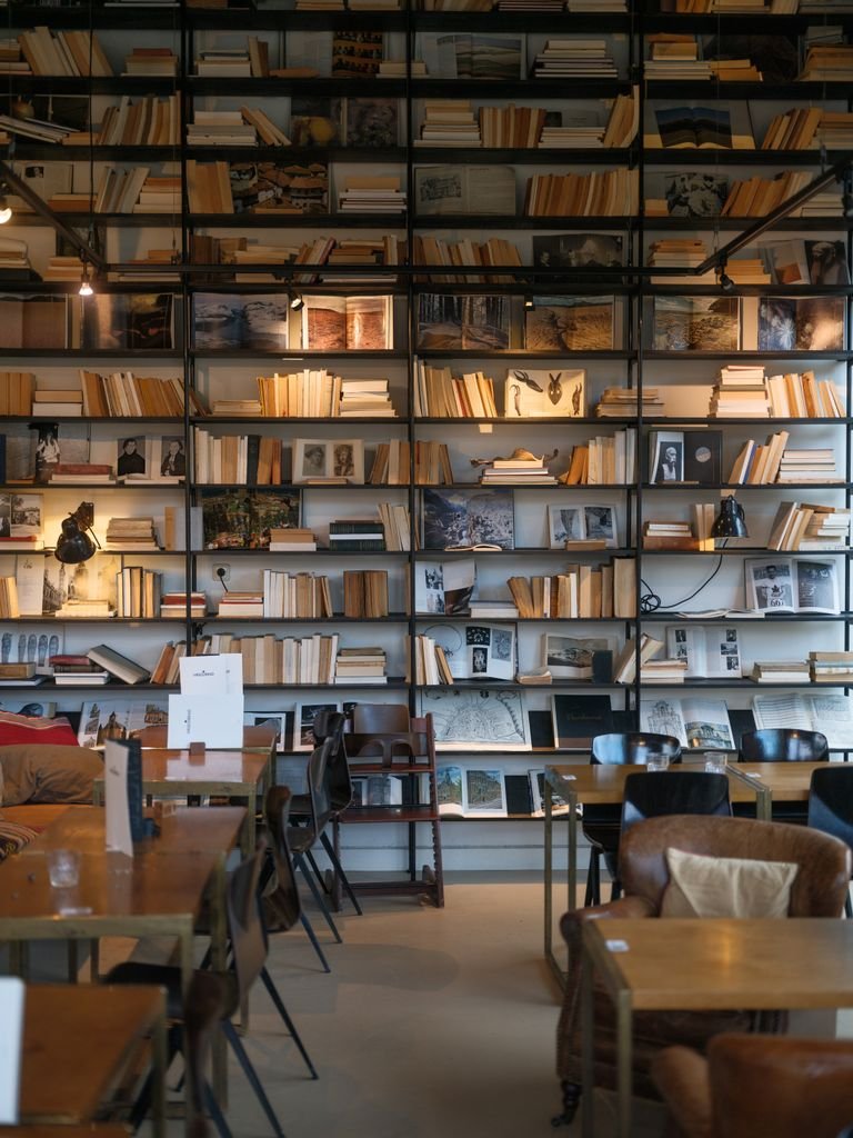 Inviting Amsterdam cafe interior featuring a wall of books and art, perfect for relaxation or reading.