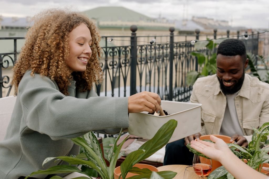 Slower lifestyle Two friends enjoying rooftop gardening with potted plants and soil, creating a joyful atmosphere.