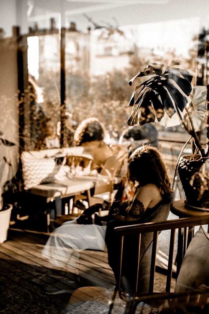 Warm-toned café interior featuring people, reflections, and potted plants, perfect for lifestyle and design themes.