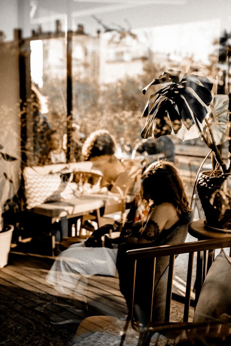 Warm-toned café interior featuring people, reflections, and potted plants, perfect for lifestyle and design themes.