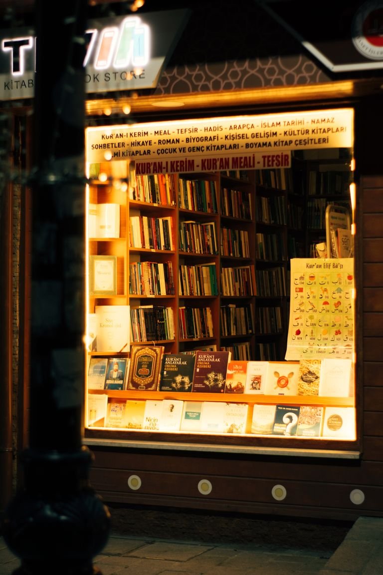 But they're the shops I find myself recommending when somebody asks where to go after they've ticked off the famous ones.Warmly lit bookstore window displaying a variety of books at night.